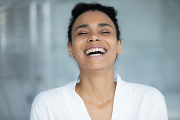 Head shot african cheerful woman in white bathrobe laughing in bathroom. Wide white perfect even toothy smile, new day positive emotions, flawless skin after home beauty treatment procedure concept