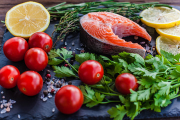 one fresh salmon steak with greenery, lemon and cherry tomatoes on the black board