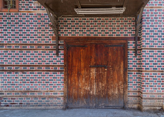 Grunge wooden decorated arched entrance gate with wooden canopy above on wall with black and red bricks with white seam