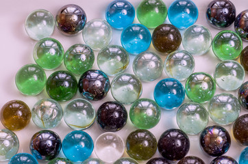 Many glass colored balls of the same size lie closely on a plane of gray color under even lighting, toned, close- up.