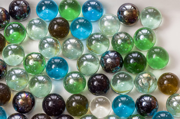 Many glass colored balls of the same size lie closely on a plane of gray color under even lighting, close- up.