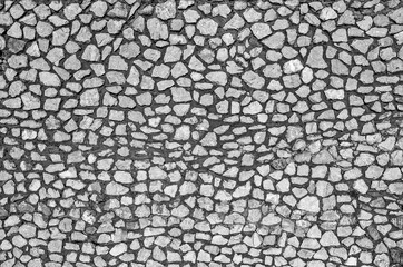 A fragment of a wall made of stones of different sizes held together with mortar, black and white, close-up, copy space.