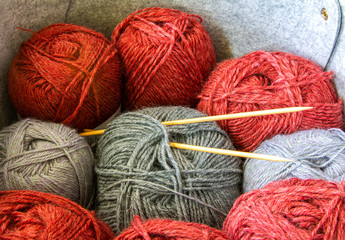 Grey and red balls of different woolen yarn with wooden knitting needles