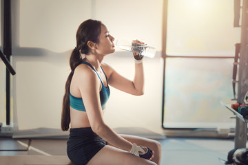 Young athletic woman drink water in gym. Refreshing in gym