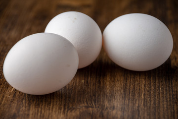 Close-up of three white eggs on dark wooden table, with selective focus, horizontal with copy space