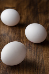 Top view of three white eggs on dark wooden table, with selective focus, vertically, with copy space