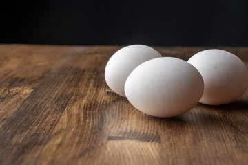Close-up of three white eggs on dark wooden table, with selective focus and black background, horizontally, with copy space