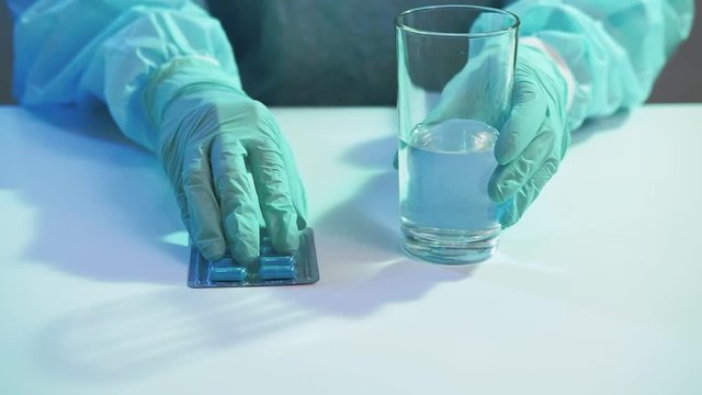 Coronavirus pandemic. Preventive medications. Nurse hands in gloves giving pills water glass.