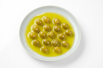 pitted green olives in olive oil in light grey plate. white background top view, closeup