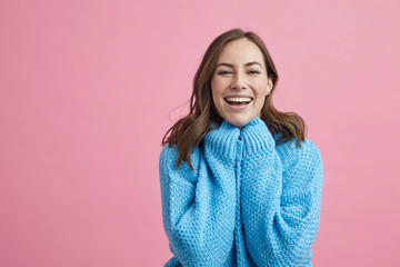 Portrait of happy and lovely young woman in a blue winter sweater on a pink background