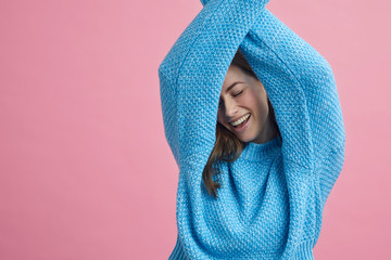 Close up portrait of attractive girl dancing in a blue sweater on a pink background