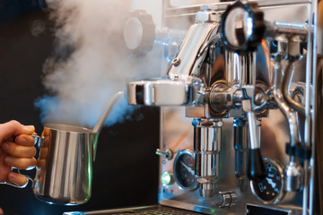 Process of preparing, brewing americano. Closeup female hands are making coffee using professional metal machine in cafe. Barista is heating milk, whipping foam with frother, steam. Hot drinks concept