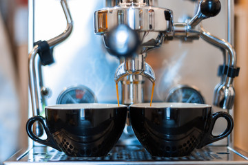 Closeup process of preparing, brewing  two black cups of espresso, americano. Barista is making coffee using professional metal steel machine in cafe, restaurant. Hot drinks, beverages concept.