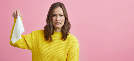 Portrait of beautiful young woman being disgusted for the tissue she is holding up 
