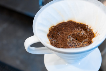 Closeup process of preparing, brewing coffee. Barista is making drink with hand drip method, pouring water on ground with filter, using special set of kettle and glass capacity. Hot beverages concept.
