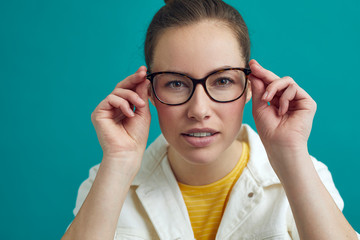 Beautiful young woman is looking into the camera / mirror to check her new glasses