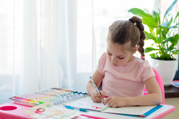 Little girl writing something in copybook and sitting at table