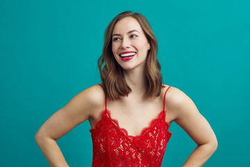 Portrait of a smiling girl in a red dress with red lipstick on ready for a date, while standing on a nice contrast background