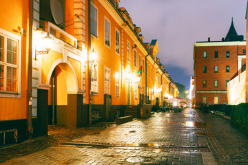 Fototapeta na wymiar Riga, Latvia. Facades Of Old Famous Jacob's Barracks And Part Of Old The City Wall In Torna Street In Lighting At Evening Or Night Illumination In Old Town.