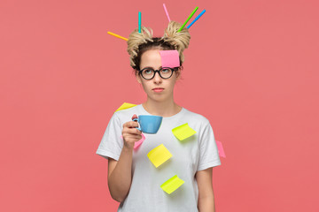 Sleepy student in a white shirt with sticky notes and markers in dreads holding cup with coffee