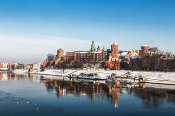 Obraz premium Ancient Royal Wawel castle on the banks of the Vistula river with tourist boats at the pier in winter, Krakow, Poland