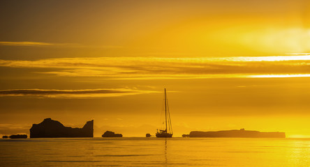 The silhouette of the sailboat and icebergs at sunset. West Greenland. Disko bay.