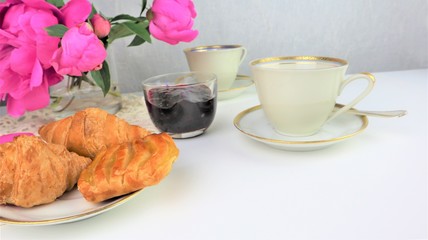 breakfast with two cups of coffee and croissants, bouquet of pink flowers