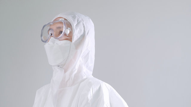 Asian Doctor In Protective Hazmat PPE Suit Wearing Face Mask And Eyeglasses, Looking Up With Copy Space