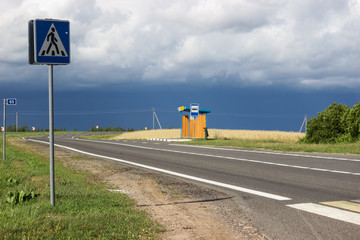 empty road and a bus stop in the middle of a ripe field before a thunderstorm