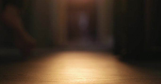 Slow motion low angle man walks with bare feet to close curtains to soften sunset light