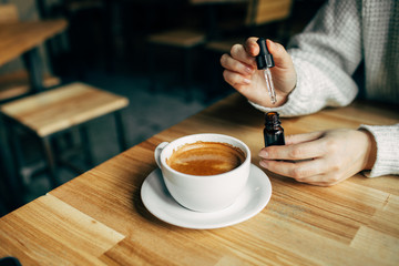 Adding CBD oil in a coffee cup. Weed supplements for a healthy food lifestyle. Woman using cannabis plants in drinks. 