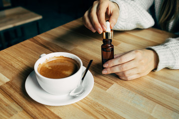  Adding CBD oil in a coffee cup. Weed supplements for a healthy food lifestyle. Woman using cannabis plants in drinks.