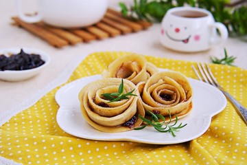 Pancakes, rolled up in the shape of a rose flower, on a white plate on a light concrete background. Pancake Day concept. Pancake Recipes. Served with plum jam