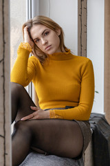 young cute girl is bored sitting on the windowsill