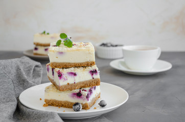 Cheesecake with black currants and streisel on a white plate with a cup of tea on a dark concrete background. Black currant cake. Delicious dessert. Horizontal orientation. Copy space.