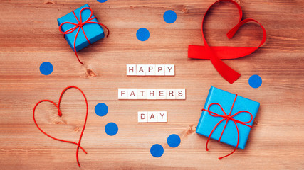 Happy fathers day words made of wooden blocks with blue gift boxes and red hearts on wooden background. Happy Father's day greeting card, holiday flat lay, top view