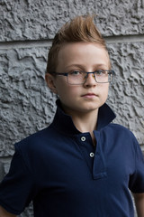  A handsome boy with glasses and a fashionable hairstyle is standing on the street wall. He is 13 years old.