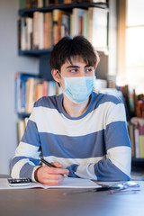 A teenaged boy wearing a face mask studying at home