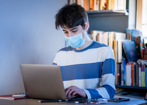 A college student wearing a face mask studying during a period of self-isolation