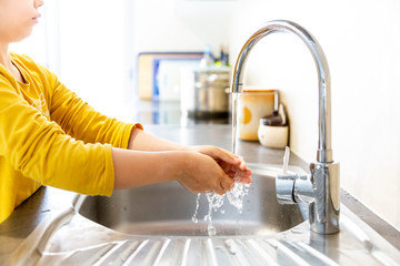 CHILD WASHING HANDS AT KITCHEN SINK