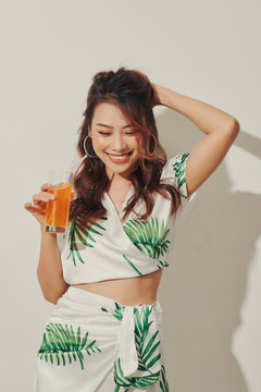 Beautiful young Asian woman with orange juice in tropical shirt on white background