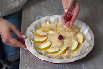 The hostess at home is preparing apple charlotte in the kitchen. puts the berry on an apple pie in...
