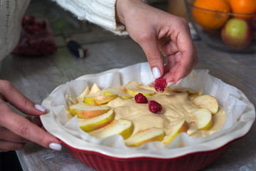 The hostess at home is preparing apple charlotte in the kitchen. puts the berry on an apple pie in a baking dish.