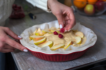 The hostess at home is preparing apple charlotte in the kitchen. puts the berry on an apple pie in a baking dish.