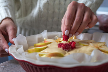 The hostess at home is preparing apple charlotte in the kitchen. puts the berry on an apple pie in a baking dish.