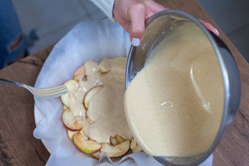 The hostess prepares apple charlotte at home in the kitchen and pours the dough into a baking dish