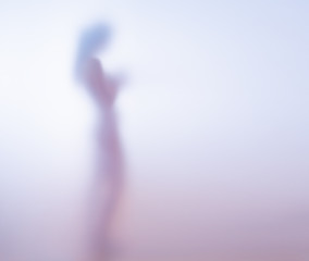 Silhouette of a naked young woman behind blurred glass