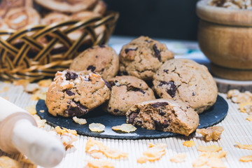 Plate with chocolate chip cookies with baskets of sweets in the background and cereals scattered on the table