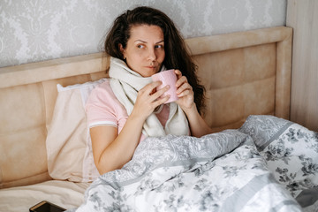 Home treatment, isolation. Sick young woman in bed drinks tea