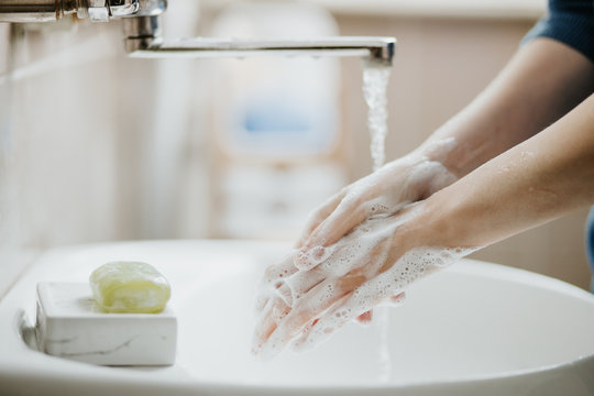Closeup of a woman washing her hands in bathroom to prevent Covid-19 viral infection. Recommended washing with soap and running water during coronavirus pandemic.